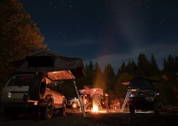 Night camping scene with SUV car tent and bonfire under starry sky