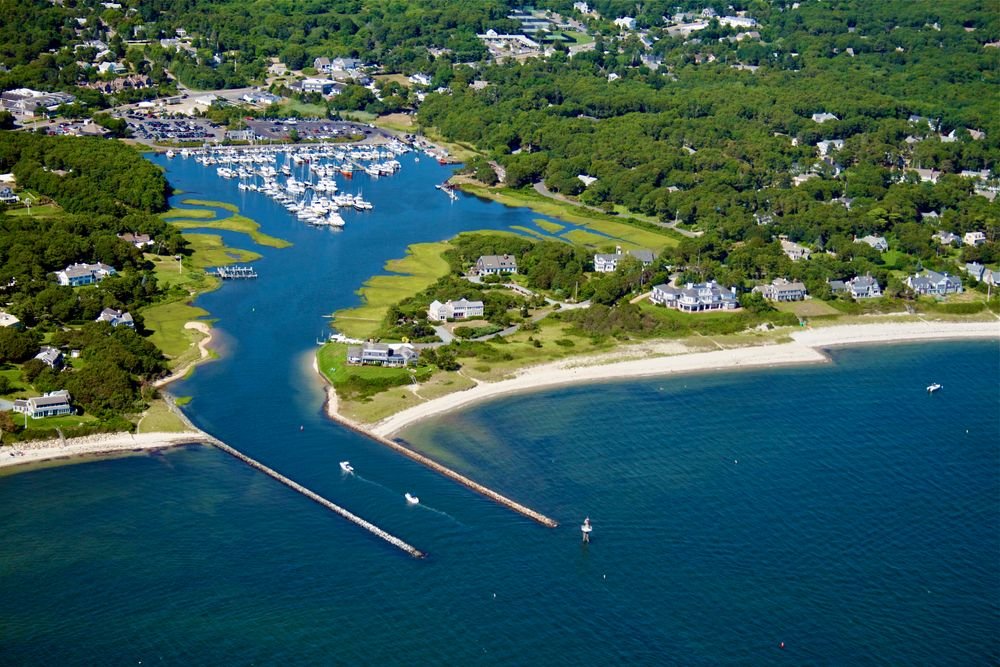 Aerial view of a coastal inlet waterway with boats, green landscape, and sandy shores in Cape Cod Massachusetts.