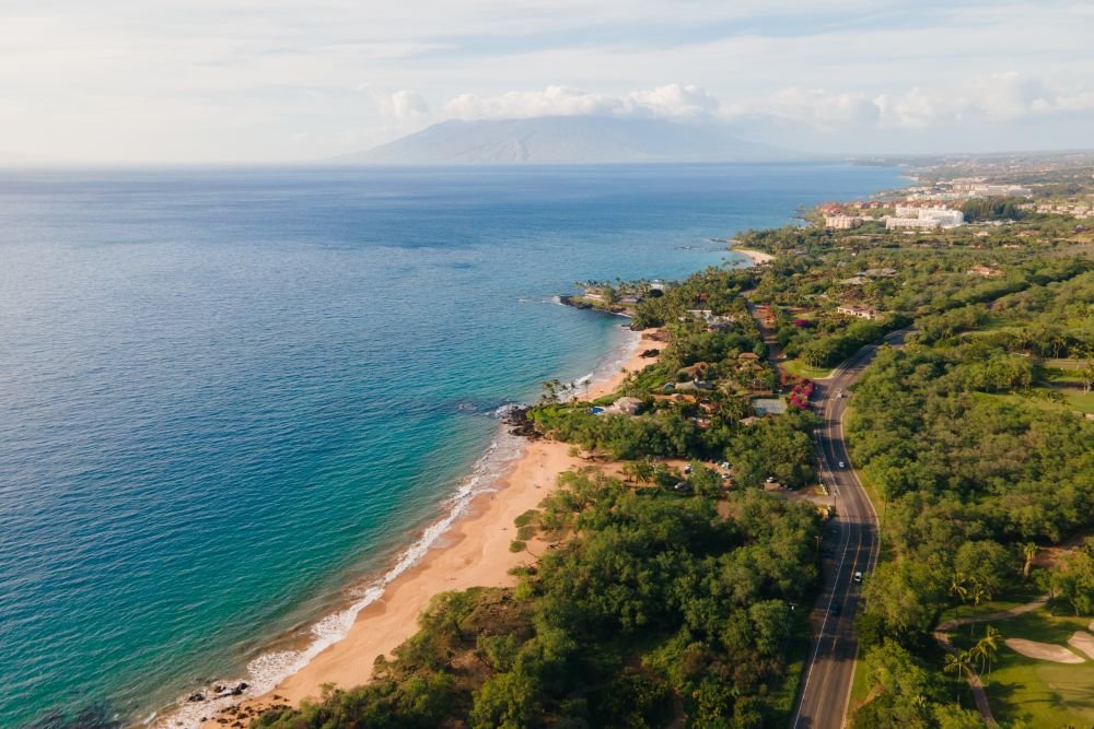 An aerial view of the sunny Maui coastline and sandy beaches, highlighting one of the best islands to visit in August for a summer vacation.