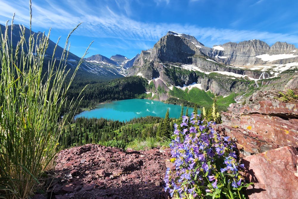 Stunning turquoise water of Grinnell Lake surrounded by rugged mountains and summer wildflowers in Glacier National Park, another candidate for the best national parks to visit in July.