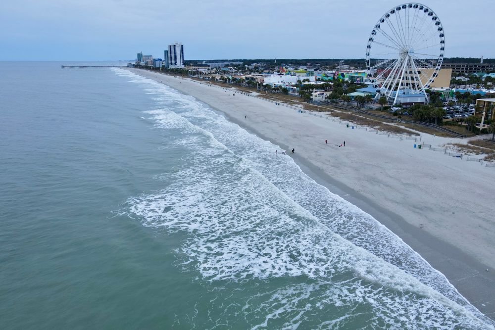 Aerial drone shot of the long sandy beach coastline and the massive SkyWheel ferris wheel at Myrtle Beach South Carolina.