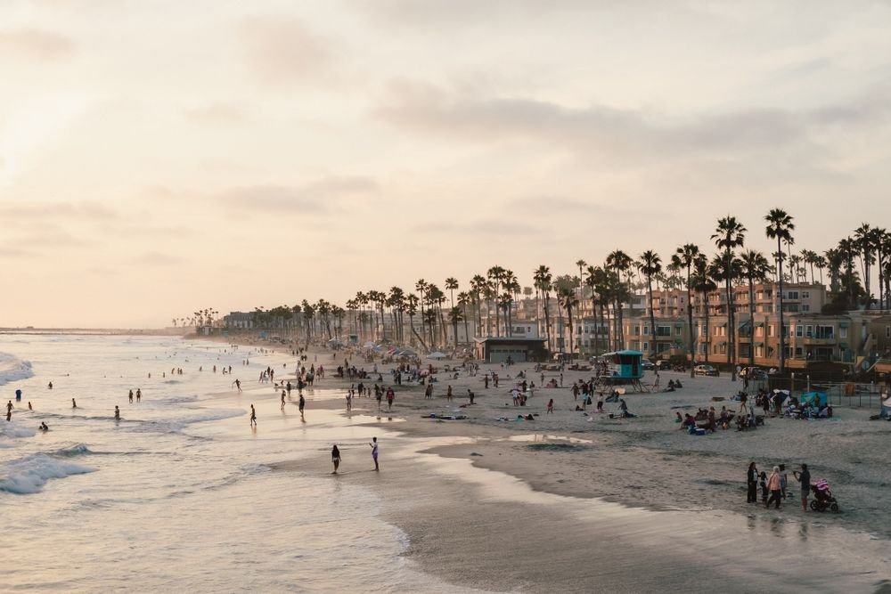 Crowded beach with palm trees and ocean waves at sunset in San Diego California.