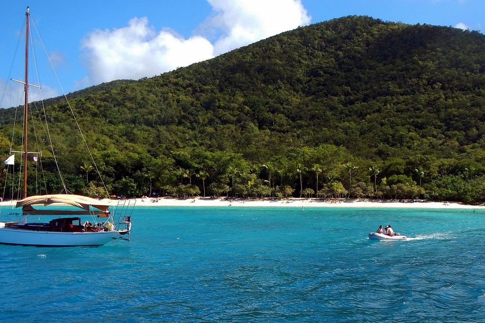 A sailboat anchored near the lush tropical shore of St. John USVI, showcasing one of the best islands to visit in August for pristine snorkeling.
