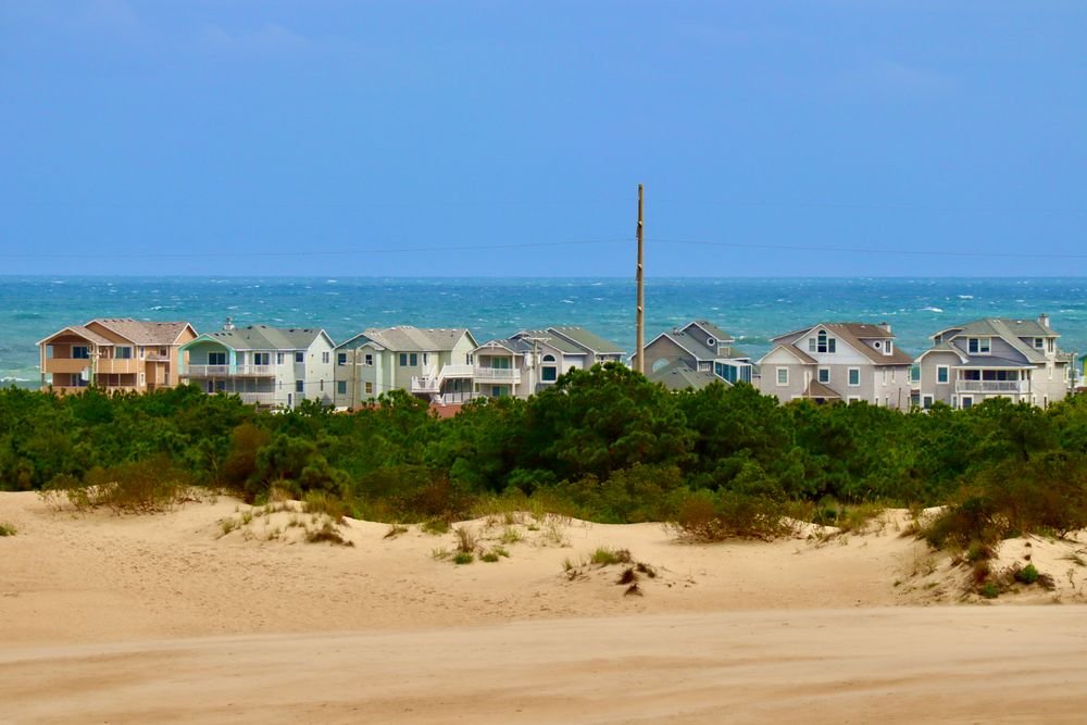 Colorful beachfront cottage houses lined up behind sand dunes and the ocean at the Outer Banks in North Carolina.